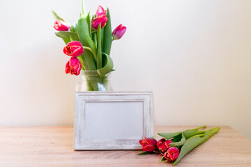 Portrait white picture frame mockup on wooden table. Modern vase with tulips.Scandinavian interior