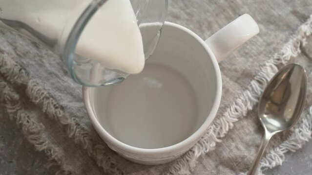 Pouring fresh milk kefir into a white cup, slow motion
