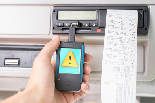 Driver holding a digital tachograph reader with an exclamation mark in a yellow triangle on the screen. Tachograph download. Control.