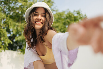Beautiful young fair-skinned lady with smile on face reaches for the camera while in fresh air....