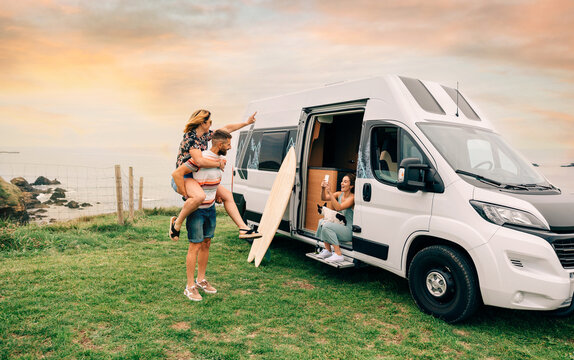 Young woman taking a photo with her cell phone of her friends having fun piggybacking next to their camper van during a trip