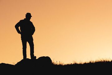 Fototapeta premium silhouette of waiting man in hat on orange background. hands to side