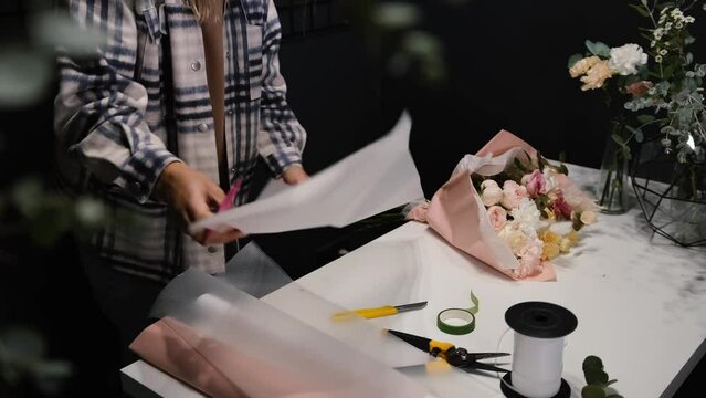 A florist cuts wrapping paper to decorate flowers. Young professional woman making flower arrangements for sale in a flower shop.