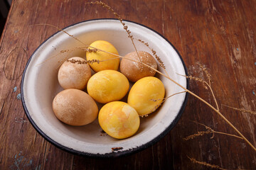 Bowl of painted Easter eggs. on wooden brown table with dry branch. Yellow and brown colored Easter eggs. Close up shot