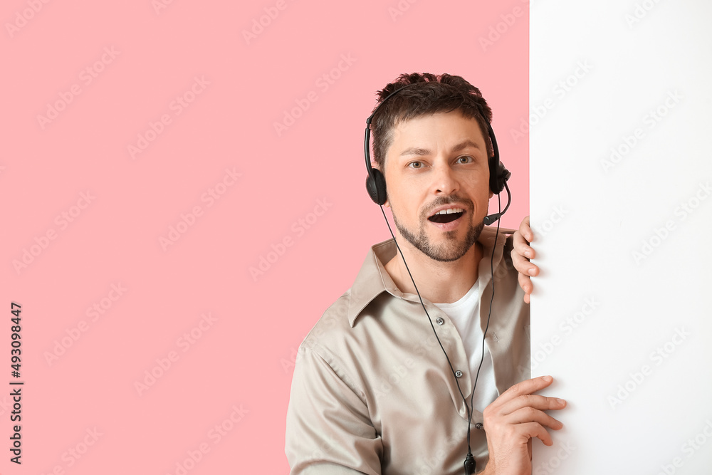 Poster surprised consultant of call center in headset with blank paper sheet on pink background