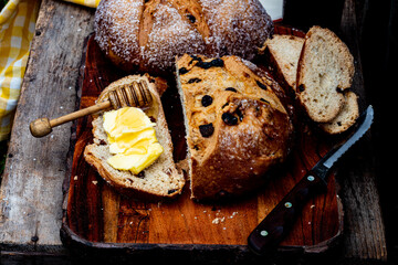 Round loaf of Irish soda bread sliced with slice of bread spread with butter and honey on a wooden dipper - 493098498
