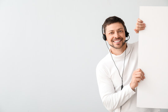 Consultant of call center in headset with blank paper sheet on light background