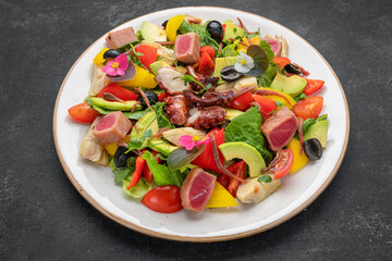 Salad with octopus, tuna and vegetables, on a dark background