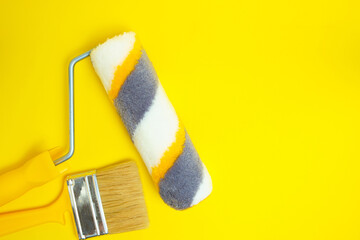 Paint roller and brush for painting and repairing walls on yellow background.