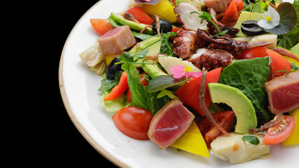 Salad with octopus, tuna and vegetables, on a dark background