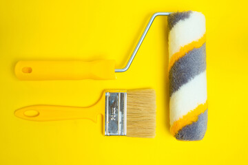 Paint roller and brush for painting and repairing walls on yellow background.