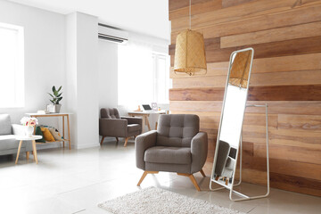 Interior of light room with armchair and mirror near wooden wall