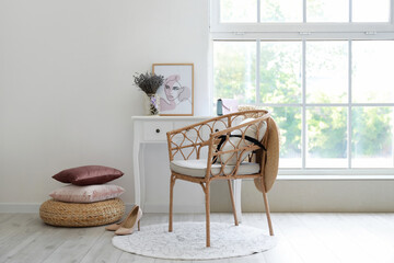 Wicker armchair with pillow and hat in interior of light room