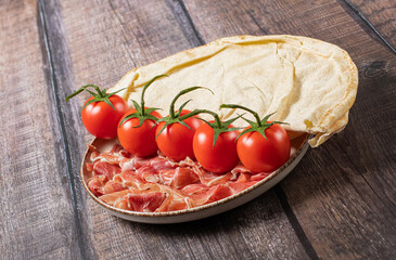 Plate with prosciutto parma, tomatoes and unleavened flatbread on a wooden background, italian breakfast, stock photo
