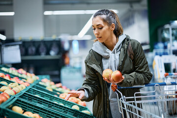 Young woman buying fruit and choosing apples in supermarket.