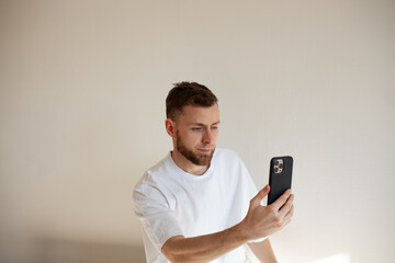 a young man with a beard 25-35 in a white t-shirt uses a smartphone