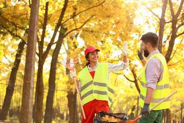 Workers giving each other high-five while gathering autumn leaves outdoors