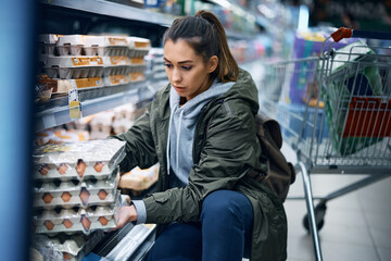 Young woman buying eggs in cardboard packaging in grocery store.
