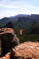 orange colored rocks in foreground with deep Blyde River Canyon green vegetation and rock formations the three rondavels in the background