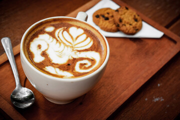 a cup of latte art coffee on a wooden table with delicious biscuits.