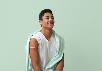 Smiling young African-American man with applied medical patch on color background