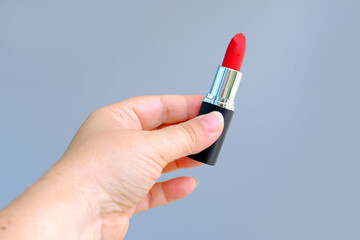 close-up female hand holding a tube with new bright red lipstick on a gray background, wants to do makeup, concept of decorative cosmetics, women's daily routine
