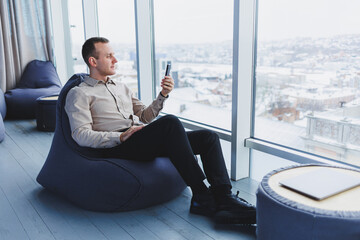 Successful male freelancer sitting in modern workspace and checking notifications on mobile phone in casual clothes. Remote work.