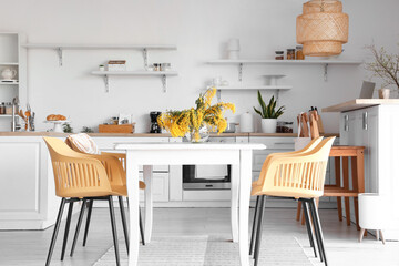 Stylish interior of light kitchen with modern furniture and mimosa flowers
