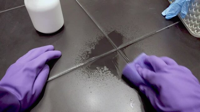 Cleaning lady clean tiled floor with detergents and washcloths. Hands in purple gloves.