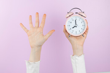 Human arm is raised up holding pink alarm clock and showing open palm, five finger on pink...