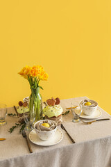 Table with beautiful setting served for Easter celebration near yellow wall