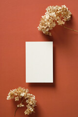 Blank vertical wedding invitation card with dried hydrangea flowers on marsala background. Flat lay, top view, copy space