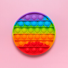 Popular silicone multi-colored anti-stress toy pop it on pink background flat lay top view. Trendy modern sensory children's toy, fidget push pop it