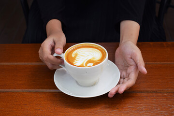 a person's hand holding a glass of coffee milk latte art on a wooden background.