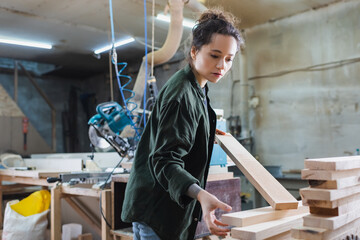 furniture designer holding wooden planks in workshop.