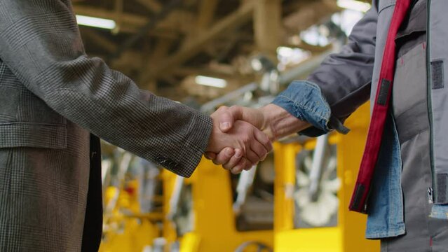Close up shot of handshake of unrecognizable engineer and worker in factory