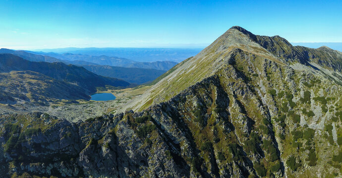 Aerial drone vertical panorama of Taul Tapului Glacier. The lake stands under the high crests of Retezat Mountains, in an alpine cauldron populated by mountain pines. Carpathia, Romania.
