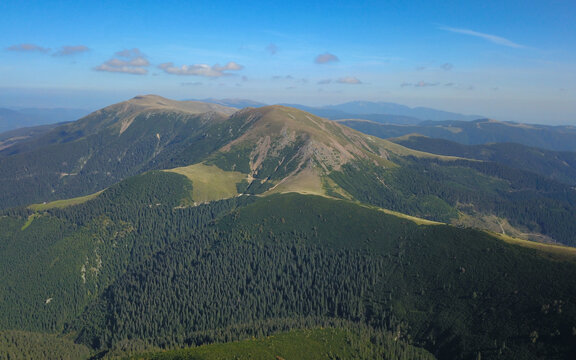 Top view above the alpine crests of Capatanii Mountains in a cloudy summer day. Clouds are casting their shadows above the green mountain pastures. Carpathia, Romania.