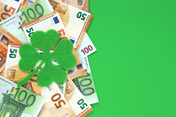Green felt four leaf clover placed on 50 and 100 euro banknotes in left half background, place for text on green paper on right side. Lucky talisman. Saint Patrick's day. Euro currency in Europe.