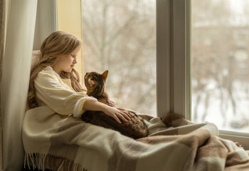 girl sits on the windowsill by the window with a cat