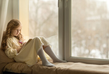 beautiful girl sits on the windowsill and writes in a notebook