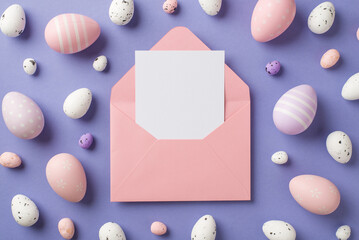 Top view of big pink envelope with card inside and many cute multicolored Easter eggs different size on the pastel violet background