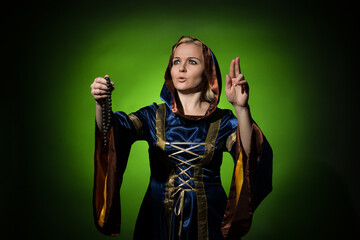 A fortune teller in a traditional dress with a rosary in her hands blesses, a portrait on a dark background, hard light