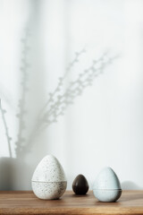 Home interior with easter decor. Pussy willow branches in a vase, easter eggs statuettes on the wooden console with light and shadow background. Minimalism, scandinavian style. selective focus.