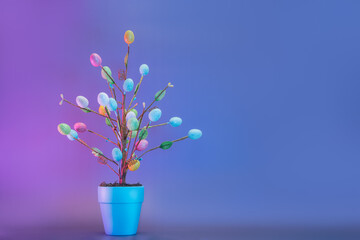 Easter tree decor in blue pot with colorful eggs in neon colors light. Purple very peri color minimalist festive background. Modern trendy Easter. Selective focus. Copy space.