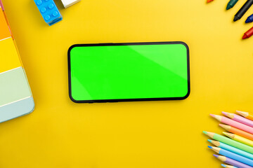 Green screen on the smartphone. Yellow background with school supplies, children's accessories, video game controller. Chroma Key