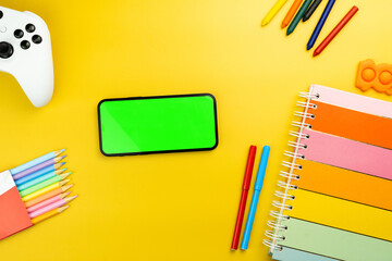 Green screen on the smartphone. Yellow background with school supplies, children's accessories,...