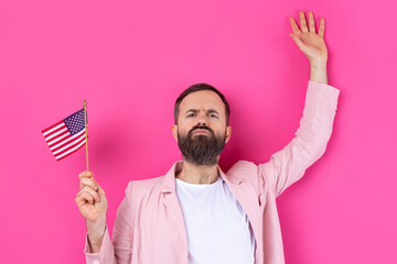 Portrait of a satisfied young man with a beard with an American flag on a red studio background....