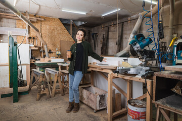 Carpenter holding paper cup near devices and equipment in workshop.