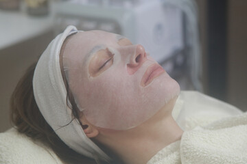 Fototapeta na wymiar Woman with facial sheet mask relaxing at beauty salon. Skin care concept. 